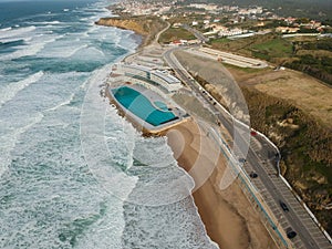 Aerial view of a big sandy beach with waves and a big ocean pool. Portuguese coastline