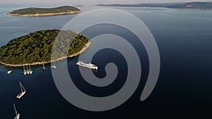 Aerial view of big white luxury yacht embarked in bay or harbour. Beautiful green island during summer season. Sailing experience