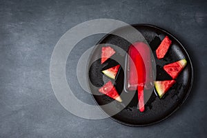Aerial view of black plate with popsicle and watermelon pieces