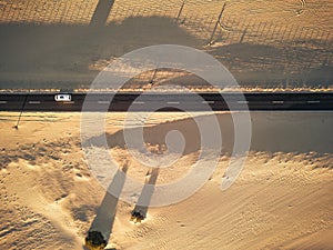 Aerial view of black straight asphalt road with sand and desert on both sides around - car traveling in the middle - concept of