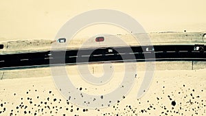 Aerial view of black straight asphalt road with sand and desert on both sides around - two car parked on the side