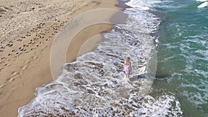 Aerial view of blonde woman strolling along seaside. Beach walk in slow motion, tranquil shore waves wash over sandy beach