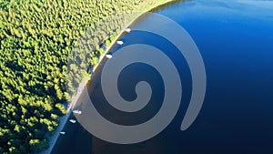 Aerial view of blue lake with a beach, boats and green forest.