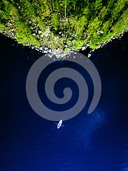 Aerial view of blue lake with a fishing boat and green forests with rocks in Finland