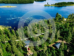 Aerial view of blue lake with green forests in Finland. Wooden house, sauna, boats and fishing pier by the lake