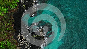 Aerial view of blue ocean and black rocks in tropics.