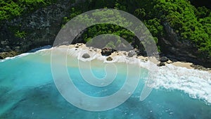 Aerial view of blue ocean with sandy beach under rocks