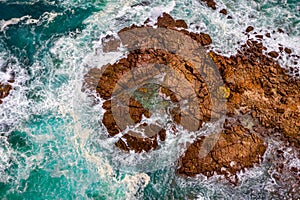 Aerial view of blue ocean surrounding etched rocks and boulders