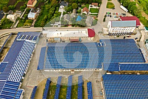 Aerial view of blue photovoltaic solar panels mounted on industrial building roof for producing clean ecological electricity.