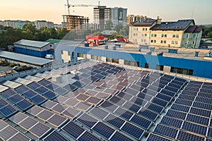 Aerial view of blue photovoltaic solar panels mounted on industrial building roof for producing green ecological