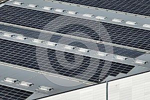 Aerial view of blue photovoltaic solar panels mounted on industrial building roof for producing green ecological