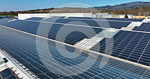 Aerial view of blue photovoltaic solar panels mounted on industrial building roof for producing green ecological