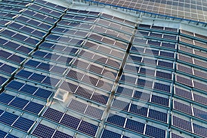 Aerial view of blue photovoltaic solar panels mounted on industrial building roof for producing green ecological