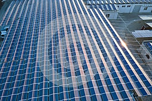 Aerial view of blue photovoltaic solar panels mounted on industrial building roof for producing green ecological