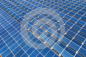 Aerial view of blue photovoltaic solar panels mounted on industrial building roof for producing green ecological