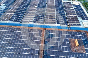 Aerial view of blue photovoltaic solar panels mounted on industrial building roof for producing green ecological