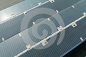 Aerial view of blue photovoltaic solar panels mounted on industrial building roof for producing green ecological