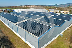 Aerial view of blue photovoltaic solar panels mounted on industrial building roof for producing green ecological