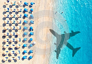 Aerial view of blue sea, airplane shadow, sandy beach, umbrellas