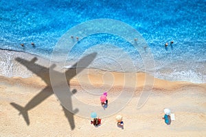 Aerial view of blue sea, airplane shadow, sandy beach, umbrellas