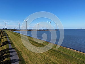 Aerial view of the blue sea and green shoreline with wind turbines in the background.