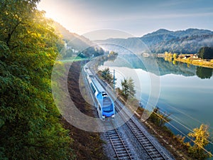 Aerial view of blue speed train moving near river in mountains