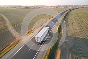 Aerial view of blurred fast moving semi-truck with cargo trailer driving on highway hauling goods in evening. Delivery