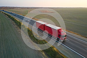 Aerial view of blurred fast moving semi-truck with cargo trailer driving on highway hauling goods in evening. Delivery