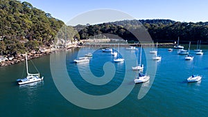 Aerial view of boats moored on Hawkesbury River, Brooklyn, Australia with blue water surrounded by eucalyptus gum trees in backgro