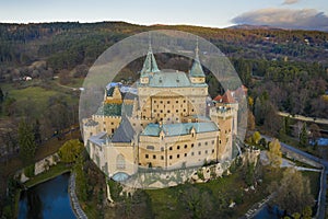 Aerial view of Bojnice castle in Slovakia guarded by its moat and surrounded by forest.