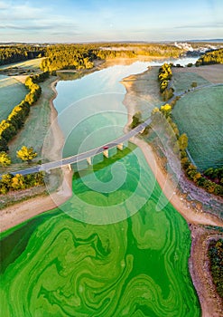 Aerial view of a bridge above the green lake surrounded by forest and agricultural fields at sunset