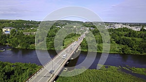 Aerial view of a bridge with driving cars above the river and green nature. Clip. Concept of transportation, bridge in