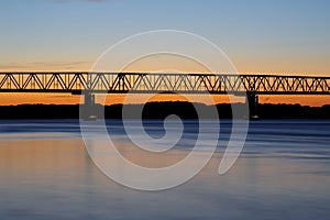 Aerial view of a bridge illuminated by a stunning sunset over a large blue body of water