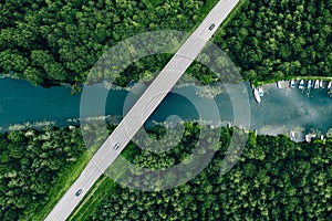 Aerial view of bridge road with car over blue river and green woods in Finland