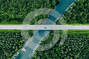 Aerial view of bridge road with car over blue river and green woods in Finland