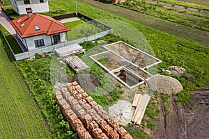 Aerial view of building site for future brick house, concrete foundation floor and stacks of yellow clay bricks for construction