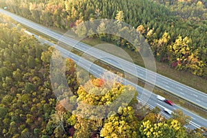 Aerial view of busy american highway with fast moving traffic surrounded by fall forest trees. Interstate transportation