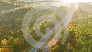 Aerial view of busy american highway with fast moving traffic surrounded by fall forest trees. Interstate transportation