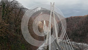 Aerial view of cable-stayed bridge between mountains at winter day, cars are moving