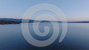 Aerial view of calm water surface in morning. Fly above Geneva lake, mountain ridge in background. Geneva, Switzerland