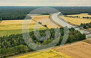 Aerial view of a canal that runs through fields, meadows and arable land in the flat landscape of northern Germany