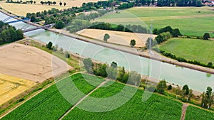 Aerial view of a canal that runs through fields, meadows and arable land in the flat landscape of northern Germany