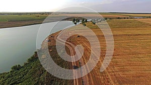 Aerial view of a car driving on a country road in between fields with a large river on one side