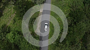 Aerial view of a car driving on a road in a green forest, shot from a flying drone, view from above