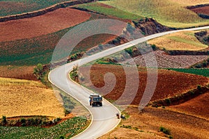 Aerial view of a car driving on a road in rural fields in red hues