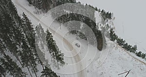 Aerial view of car driving among the winter forest covered with snow.