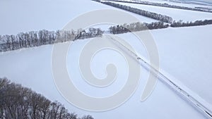 Aerial view on car driving through winter forest road between the snow-covered fields