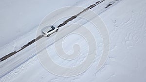 Aerial view on car driving through winter forest road between the snow-covered fields