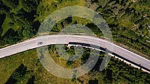 Aerial view of car on the move on road amidst lush green forest. Car passing on road through beautiful green forest cover. Top