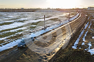 Aerial view of car moving along muddy rural road in bad condition on sunny spring or winter day